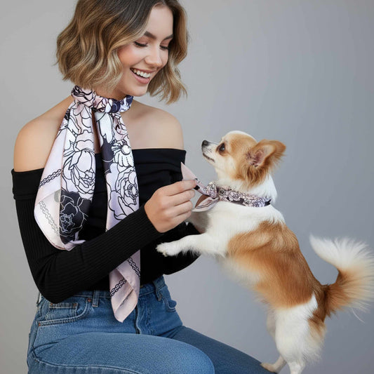 Woman holding a small dog wearing matching scarves against a gray background