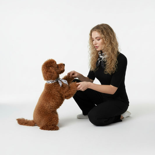 Woman in black outfit kneeling on a white floor with a brown dog wearing a bandana.