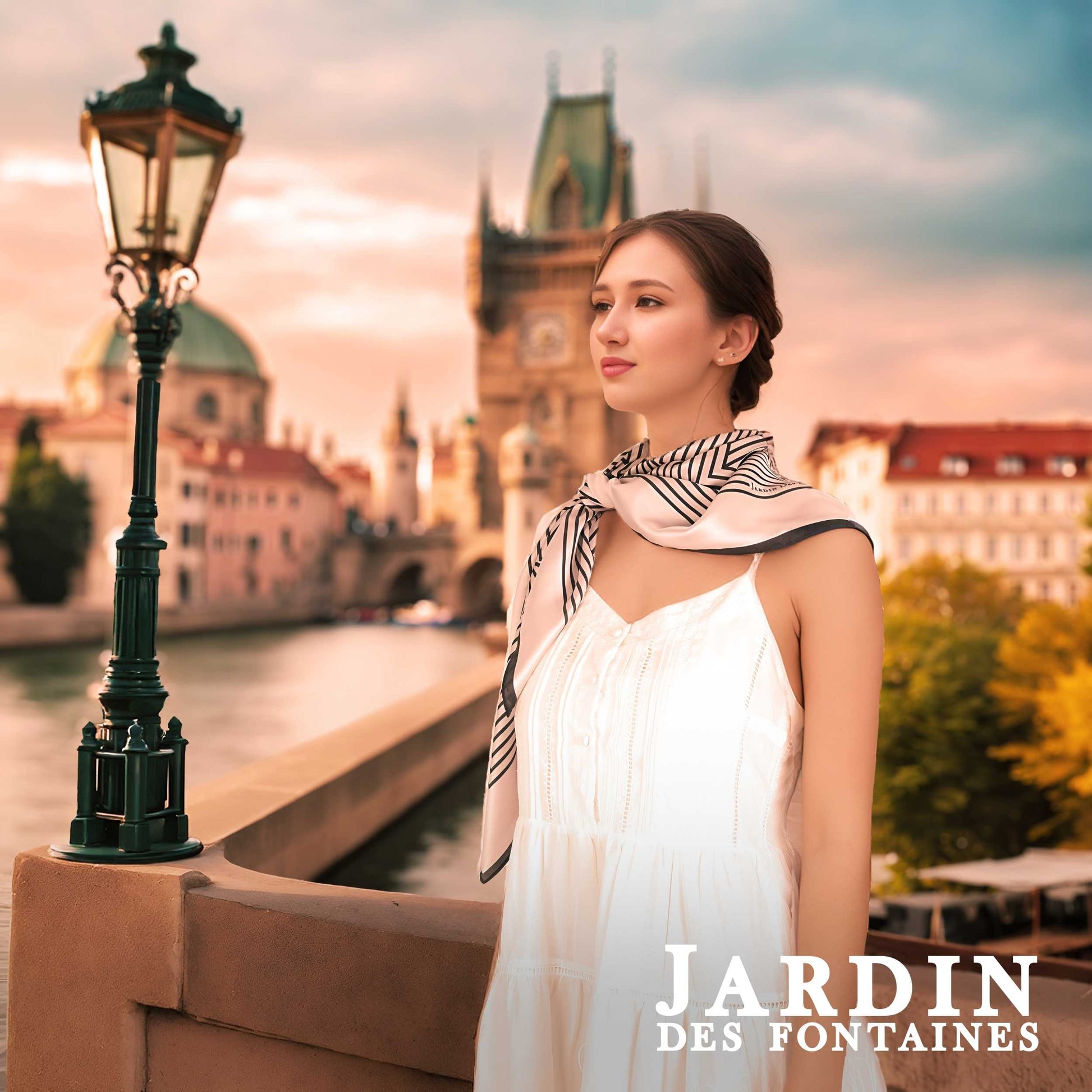 Woman in a white dress with a zebra-patterned scarf standing by a river with a cityscape in the background, featuring 'Jardin des Fontaines'.