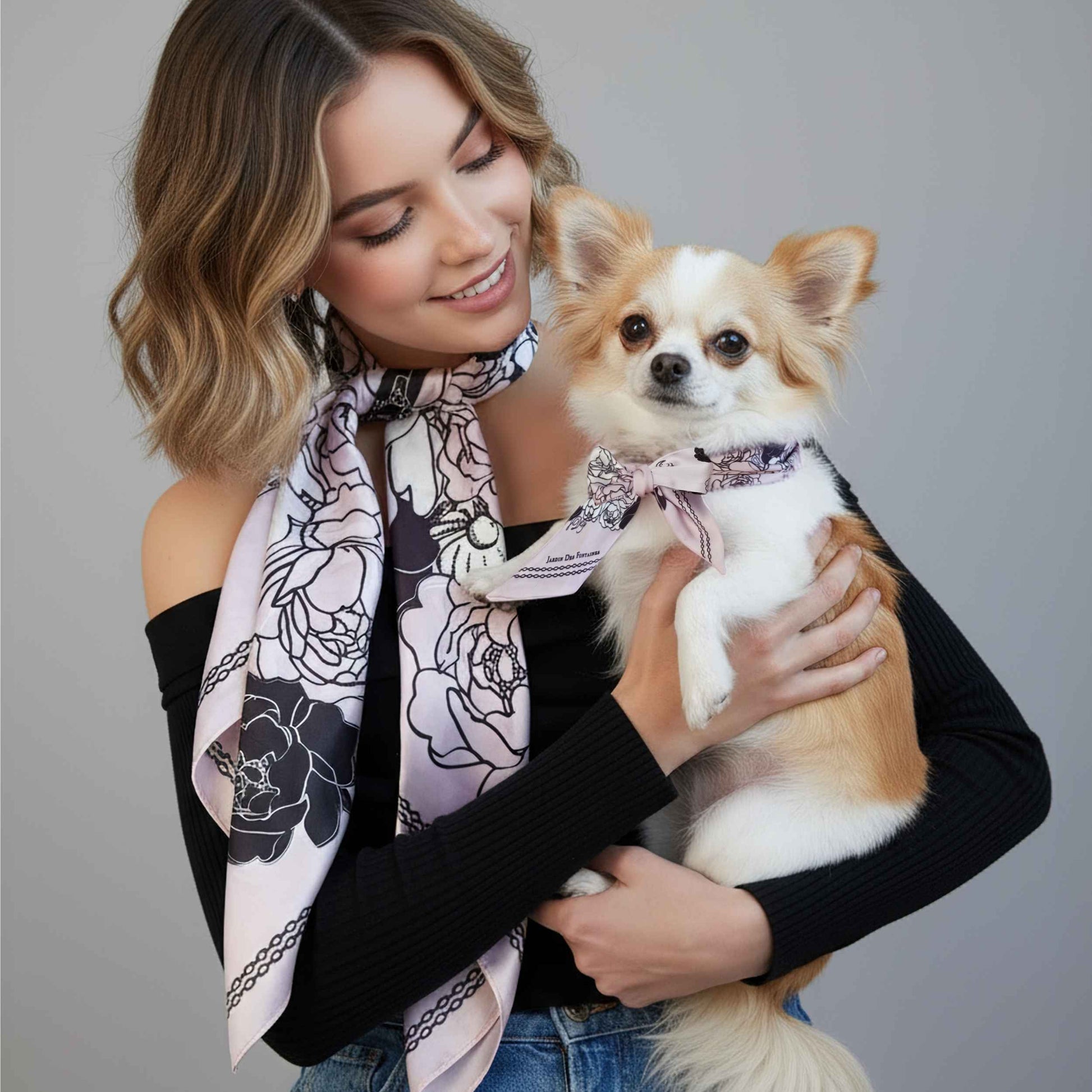 Woman holding a small dog wearing a matching scarf against a gray background