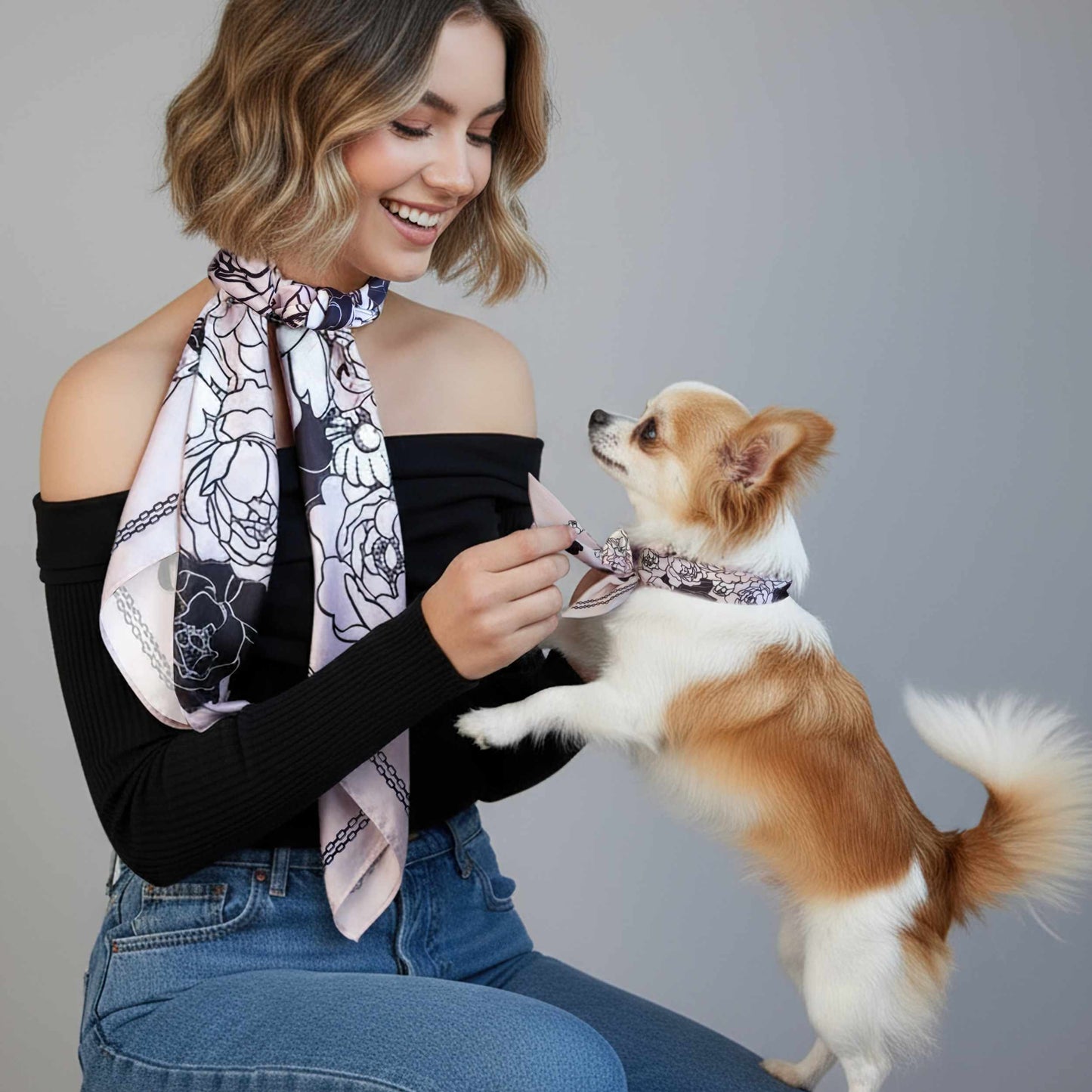 Woman holding a small dog wearing matching scarves against a gray background