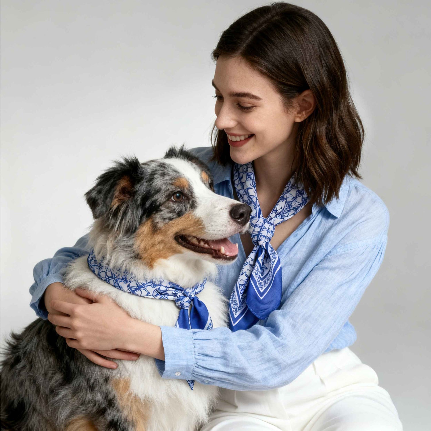 Woman holding a dog both wearing blue bandanas against a plain background